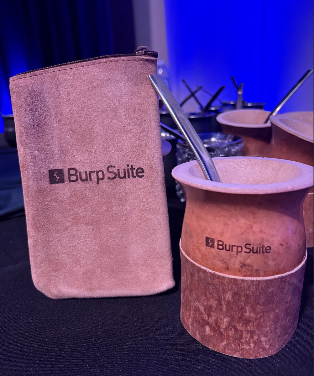 A Burp-Suite-branded yerba mate cup with stainless steel bombilla, beside a branded suede pouch at EkoParty Buenos Aires