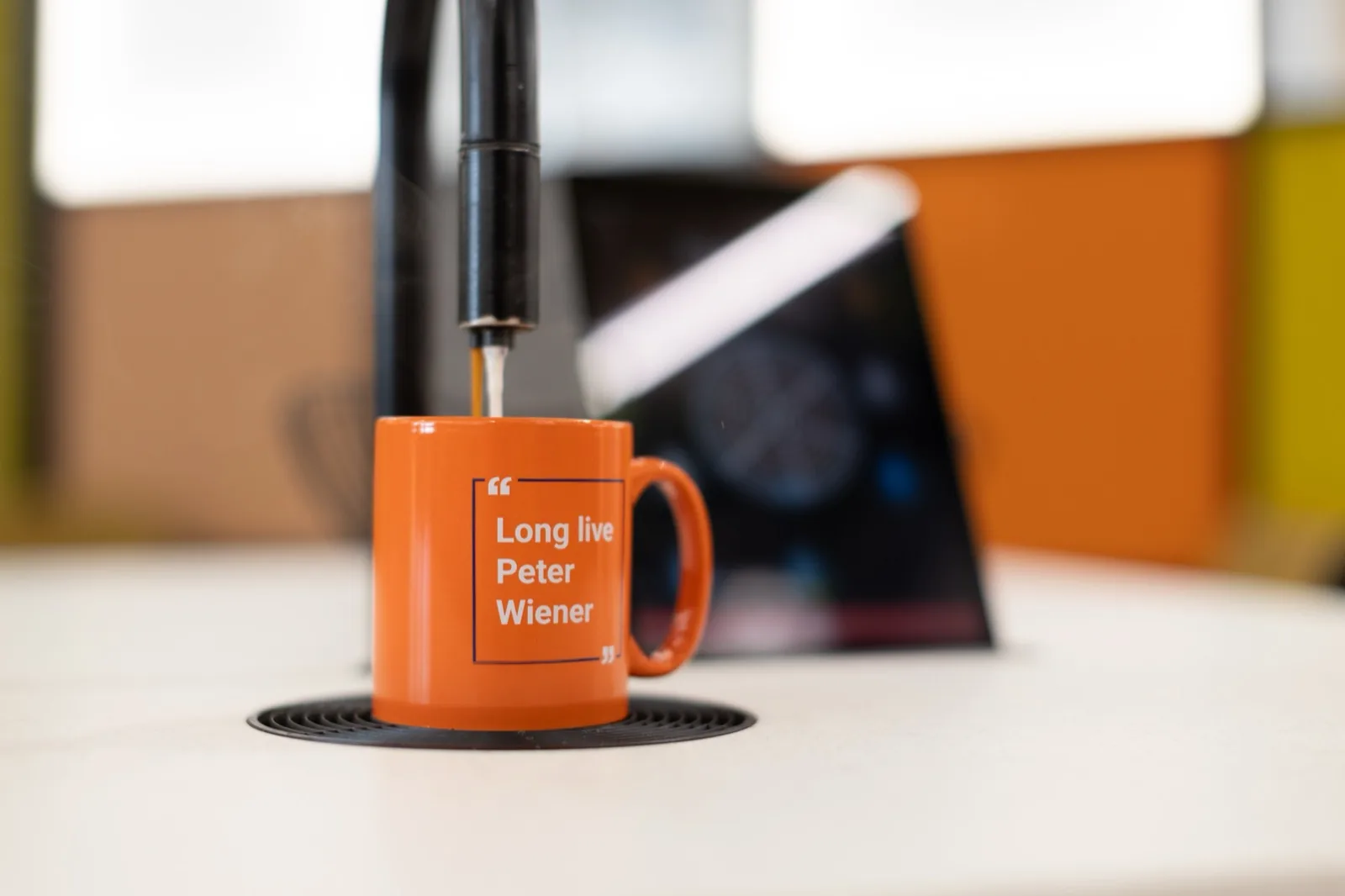 A coffee tap dispensing espresso into an orange mug reading "Long live Peter Wiener" — a nod to Knutsford office culture