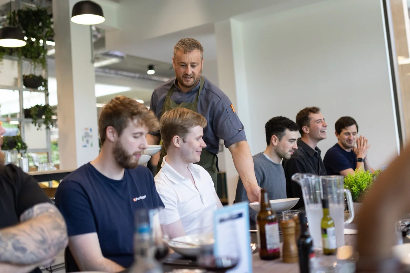 Swiggers dining together at a Knutsford fine-dining event — a chef serves at the table while colleagues laugh further down