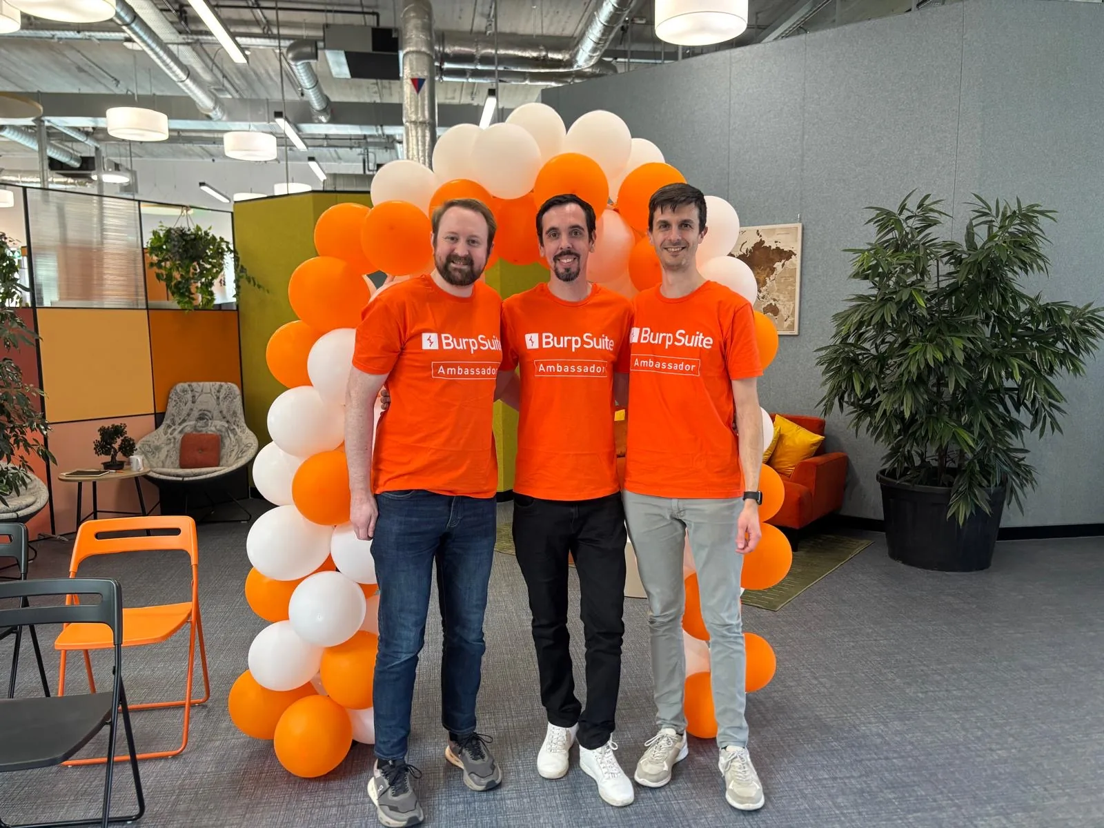 Three Burp Ambassadors — Tib3rius, Alan Levy, and Federico Dotta — standing in Burp t-shirts in front of a balloon arch at the program launch