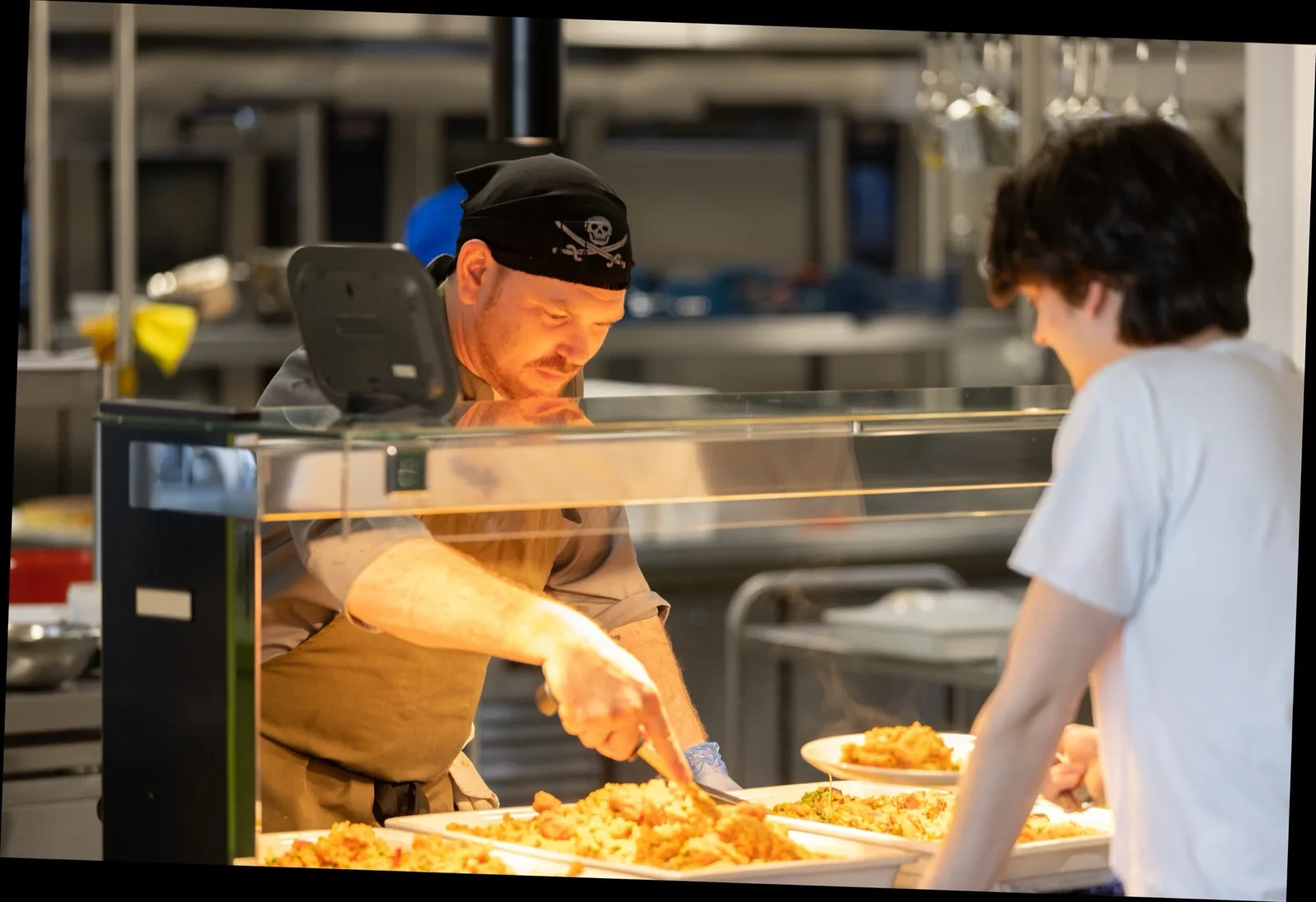 The Kitchen at the Knutsford office — long communal tables under warm lighting, lunch in service